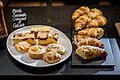 Auf schwarzen Granitplatten sind Croissants angerichtet und auf einem weißen Teller daneben befinden sich lauter kleine süße Teilchen. Dahinter ist die übliche Tafel mit der Beschriftung zu sehen.