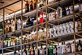 Wein- und Cocktailgläser, daneben zahlreiche Wein- und Schnapsflaschen in einem offenem Regal zu bestaunen.