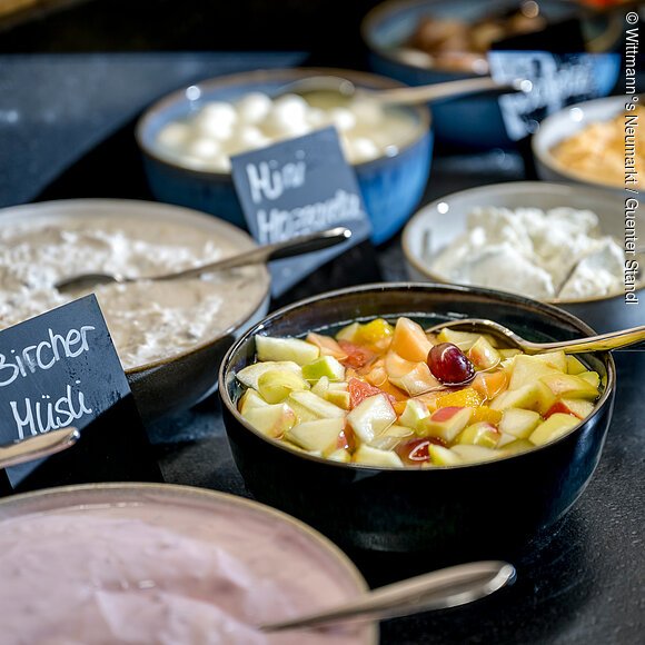 Frühstücksbuffet im Wittmann°s Neumarkt Schwarze Schüsseln gefüllt mit Bircher Müsli, Erdbeerjoghurt, Obstsalat und Quark angerichtet auf einem Tisch.