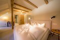 Das helle Bett steht mitten im Zimmer und ist mit Kissen verziert, der Raum hat eine Holzbalkendecke.
