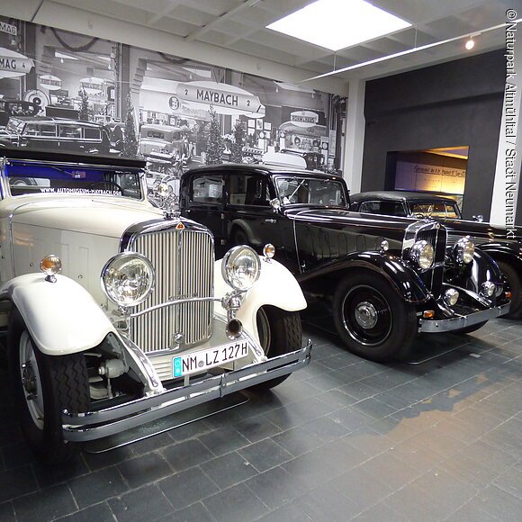 Maybach-Museum Neumarkt Drei Oldtimer-Autos nebeneinander in einem Museum mit historischem Schwarz-Weiß-Foto im Hintergrund.