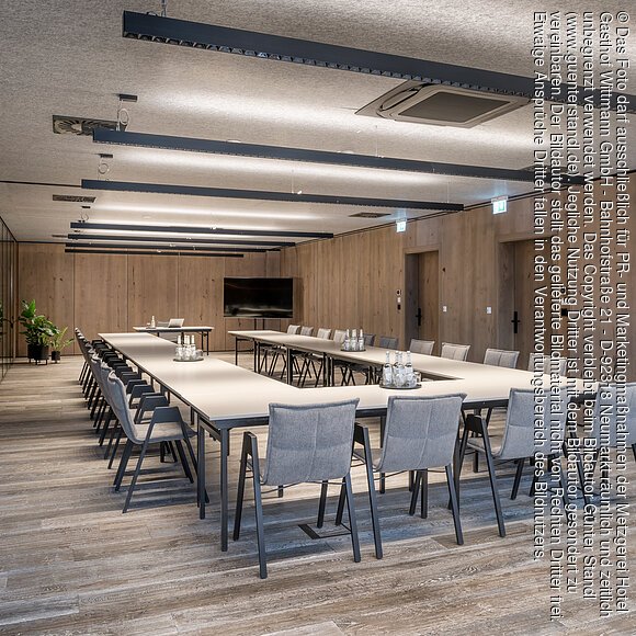 Großer Tagungsraum im Wittmanns Neumarkt Konferenzraum mit U-förmigen Tischen, grauen Stühlen, Holzwänden und Deckenleuchten.